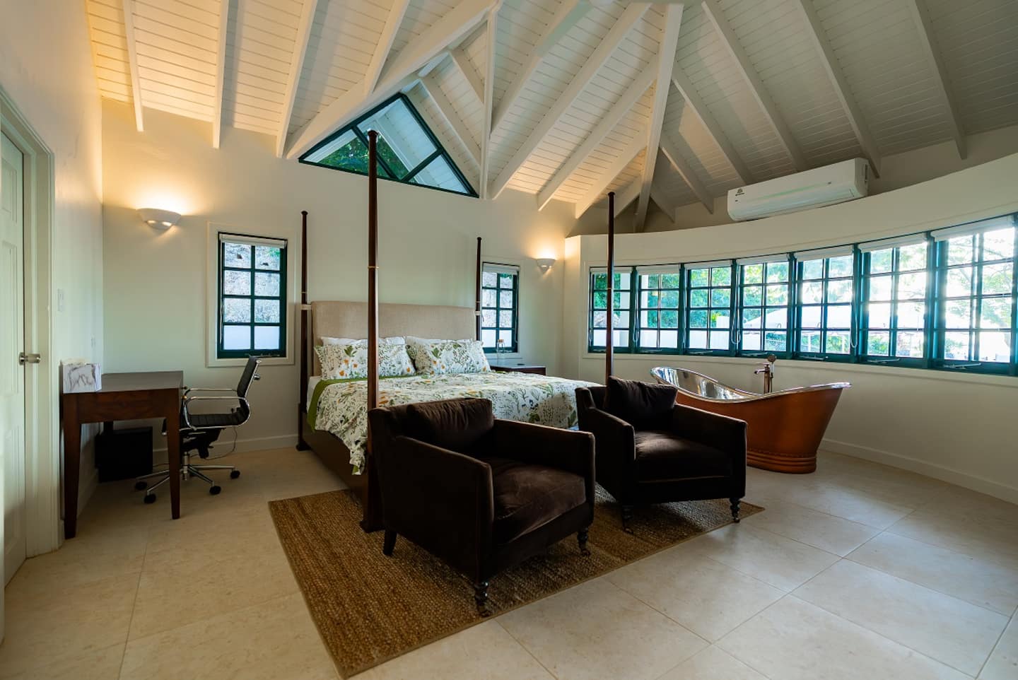 Spacious primary bedroom with vaulted ceiling and green framed windows